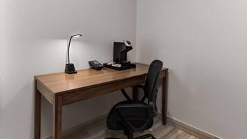 A corner office with a wooden desk, two black office chairs, a desk lamp, a telephone, and a small black object on the desk.