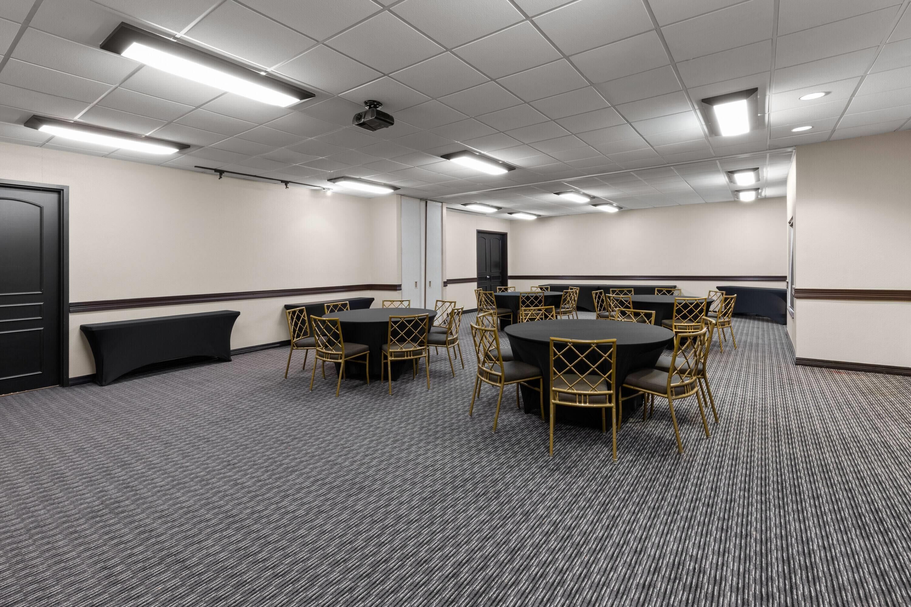 A conference room with round tables, chairs, a black bench, and a door.
