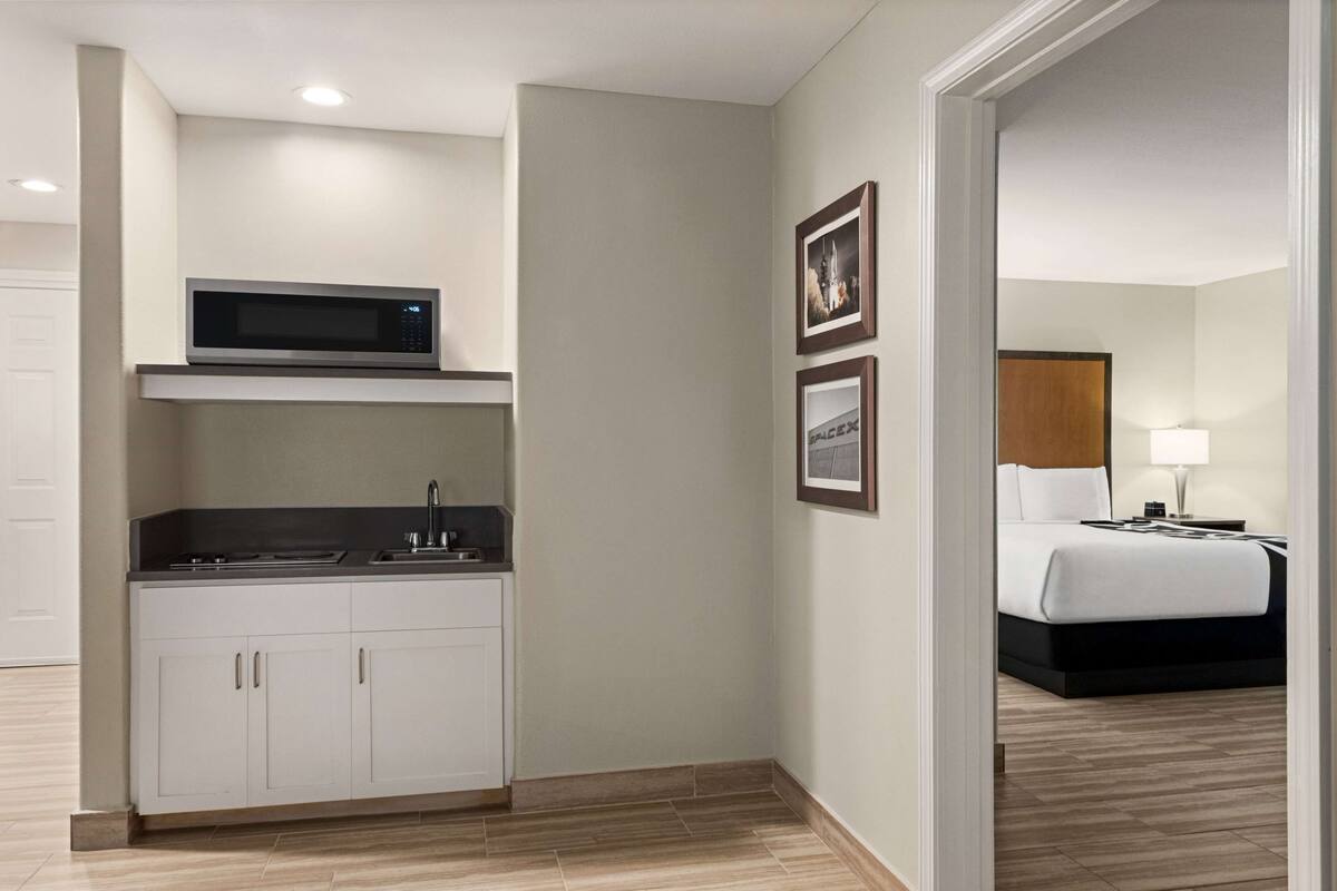 Ein Hotelzimmer mit einer Küchenzeile, einem Bett, einem Nachttisch und gerahmten Bildern an der Wand.