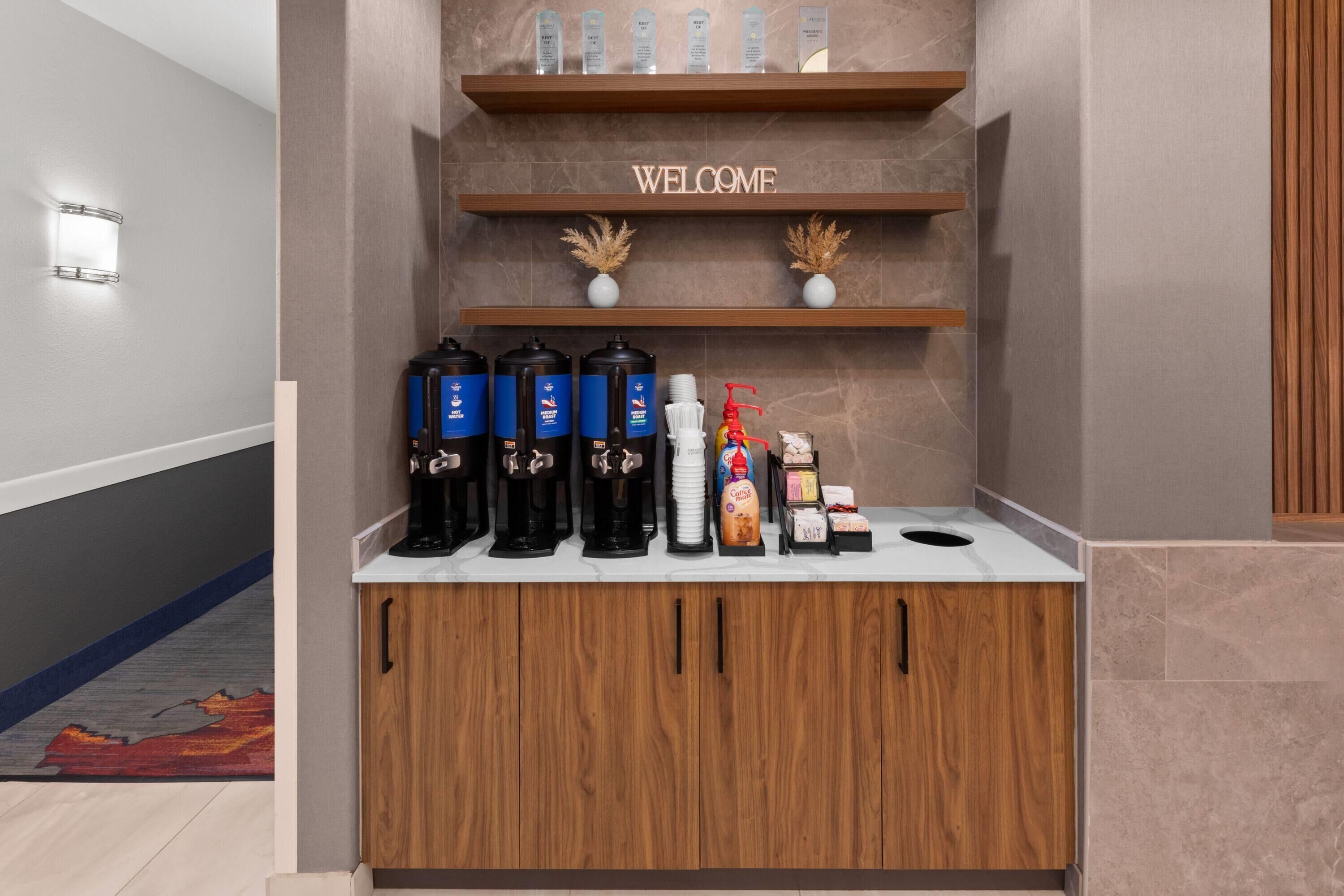A reception area with a 'WELCOME' sign, coffee machines, and a counter with various items.