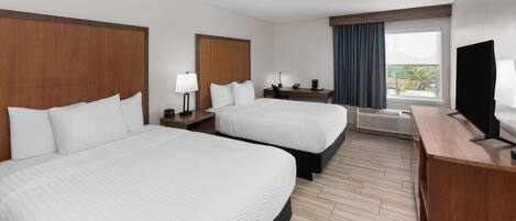 A hotel room with two beds, a desk, a TV, and a window with curtains.