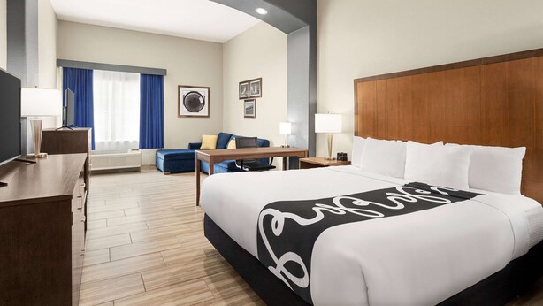 A hotel room with a large bed, a desk, a chair, a sofa, and a TV. - La Quinta Inn & Suites by Wyndham Brownsville North (Brownsville)