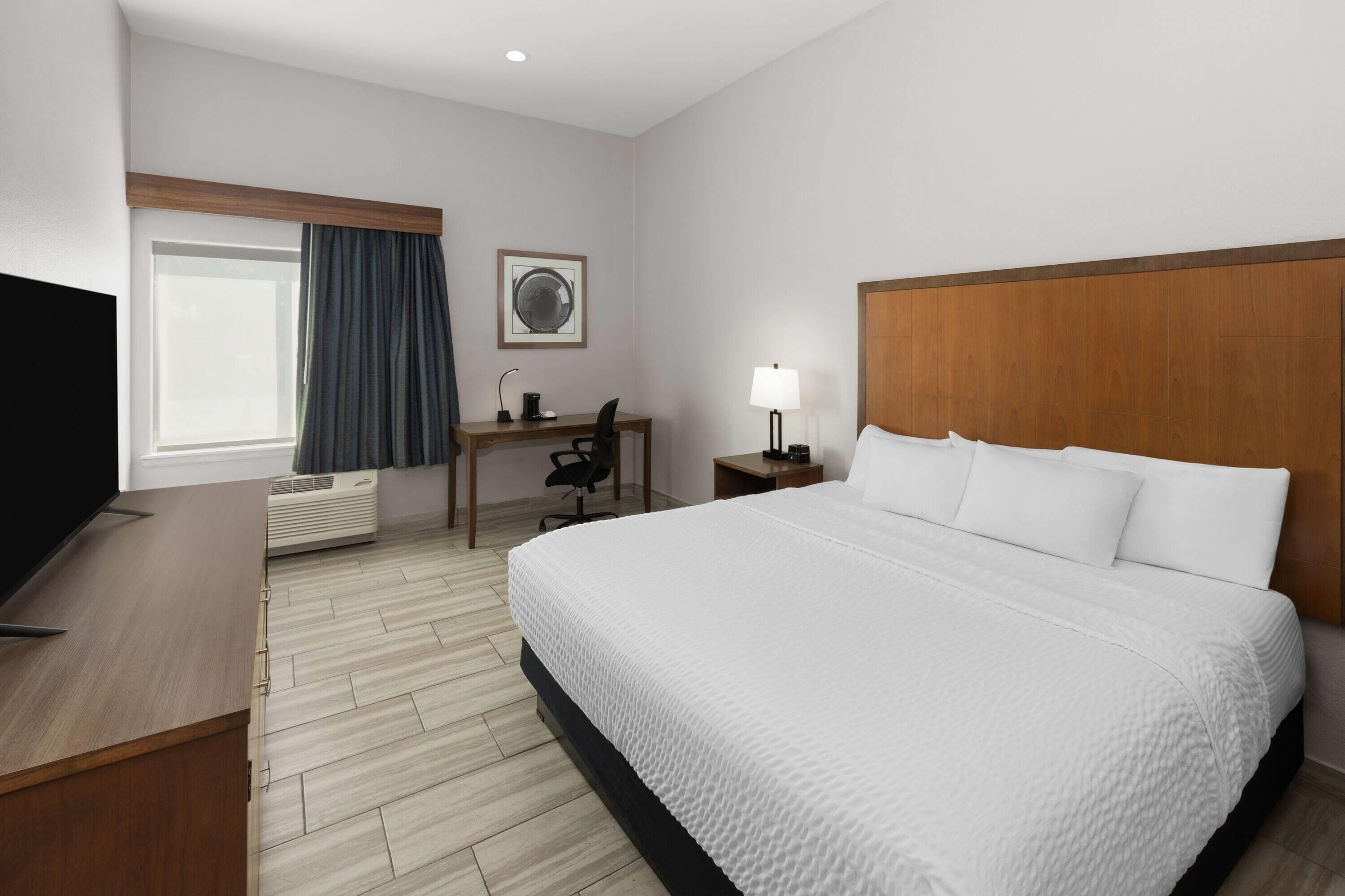 Una habitación de hotel con cama, escritorio, silla, televisor, lámpara y aire acondicionado.