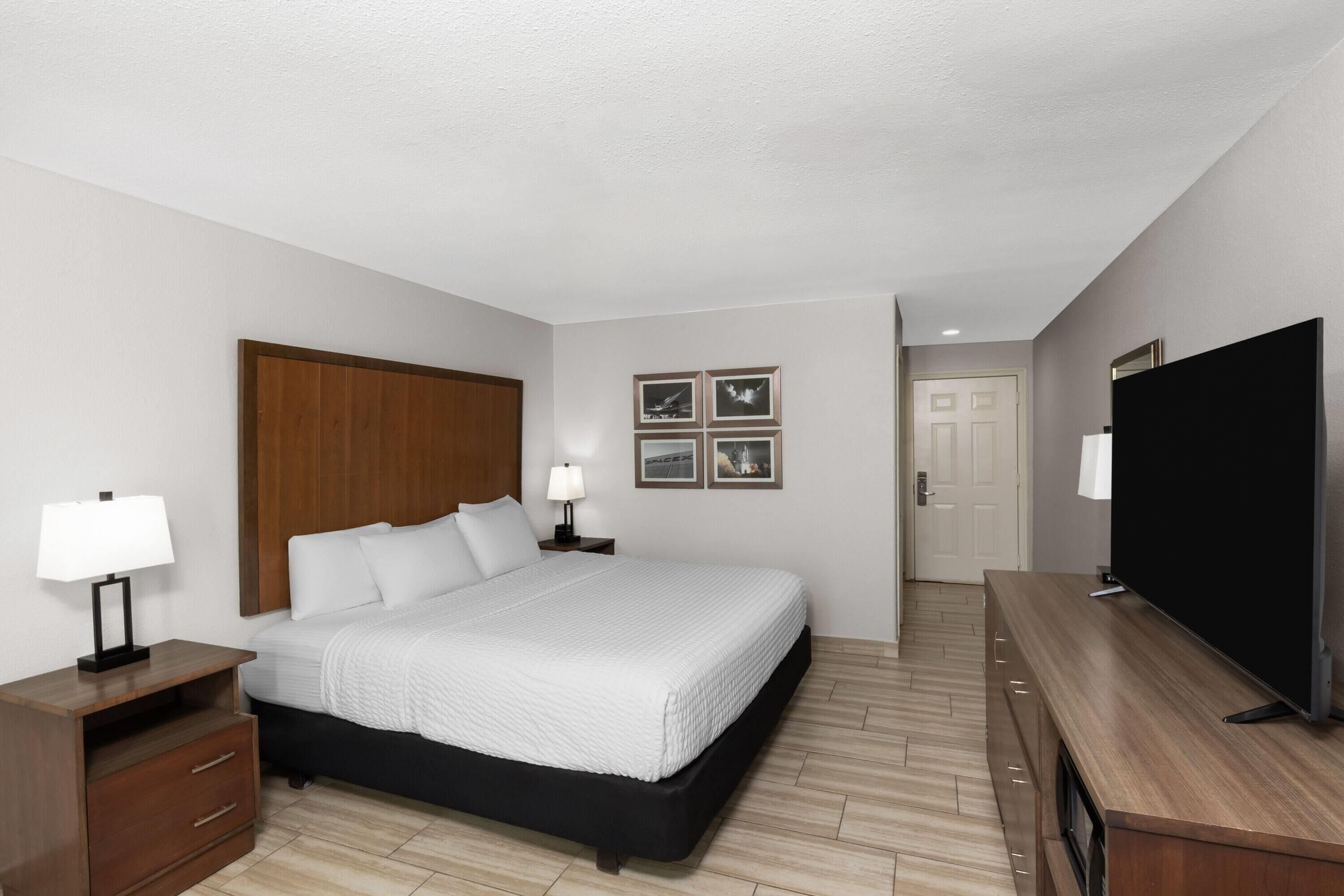 A hotel room with a bed, nightstands, a TV, and framed pictures on the wall.