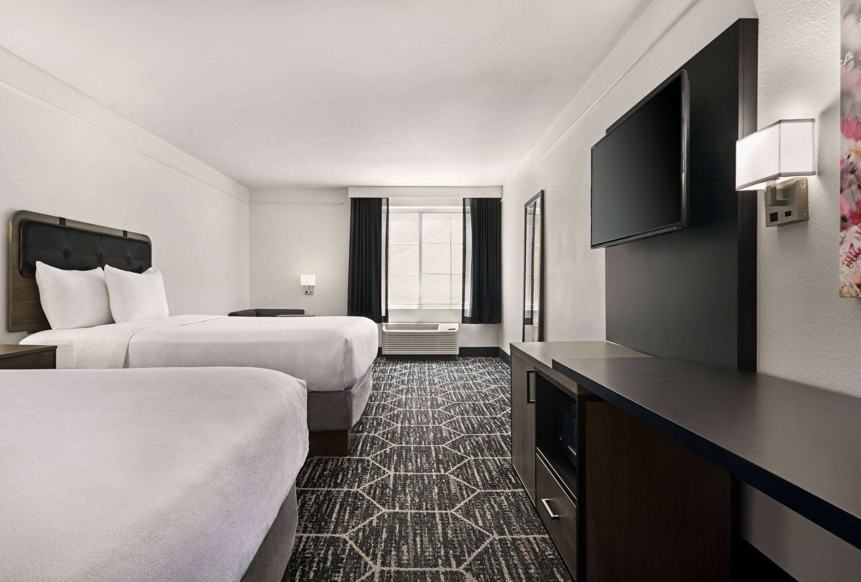 Habitación de hotel con dos camas, televisión, escritorio y ventana con cortinas.