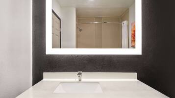 A bathroom with a white sink, a mirror, and a shower area.