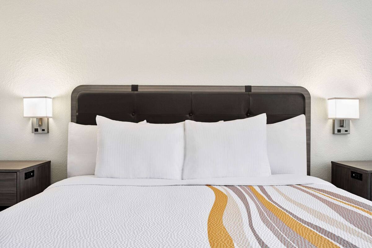 A hotel room with a large bed, two bedside tables, and two wall-mounted lamps.
