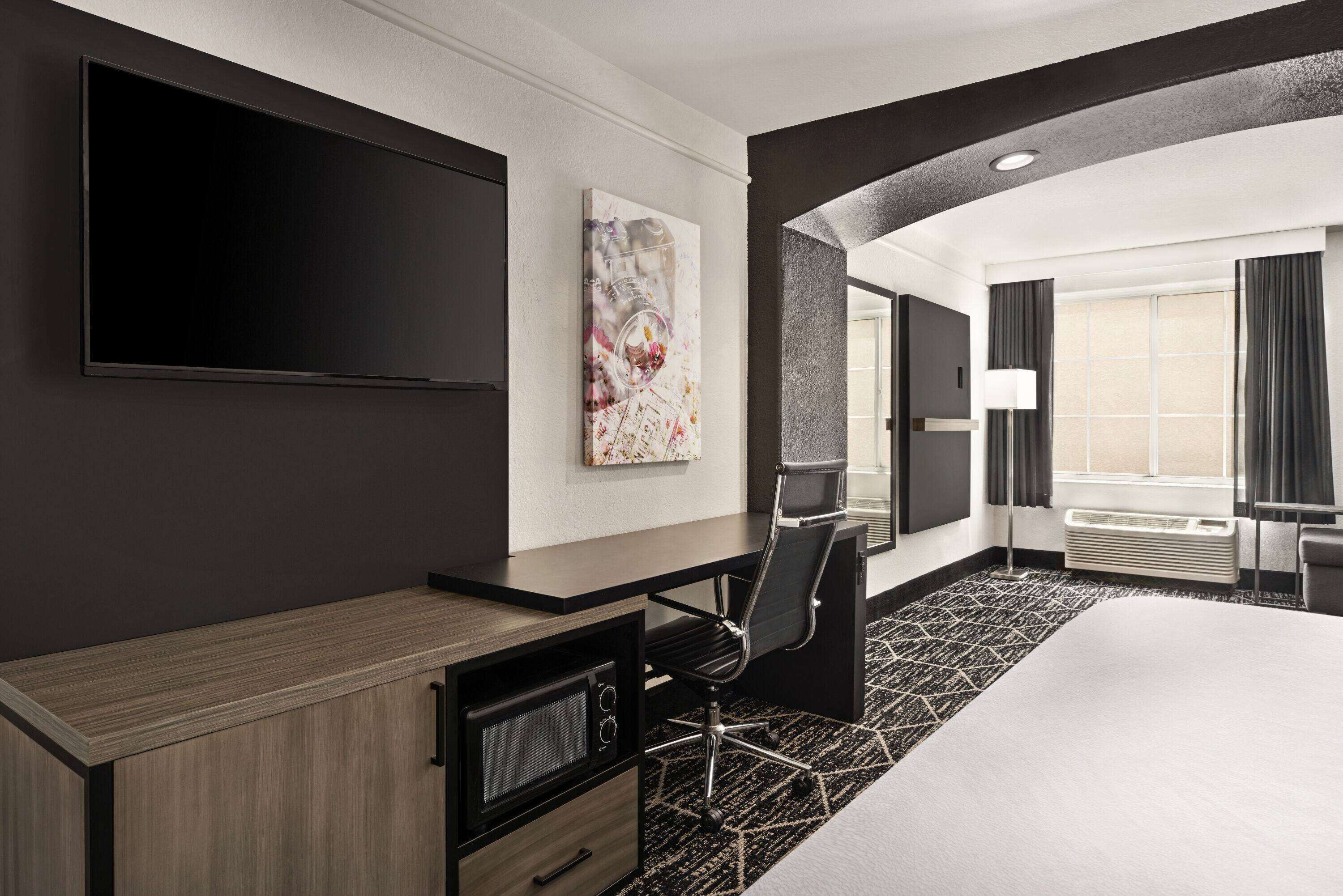 A hotel room with a bed, a desk with a flat-screen TV, a microwave, and a chair.
