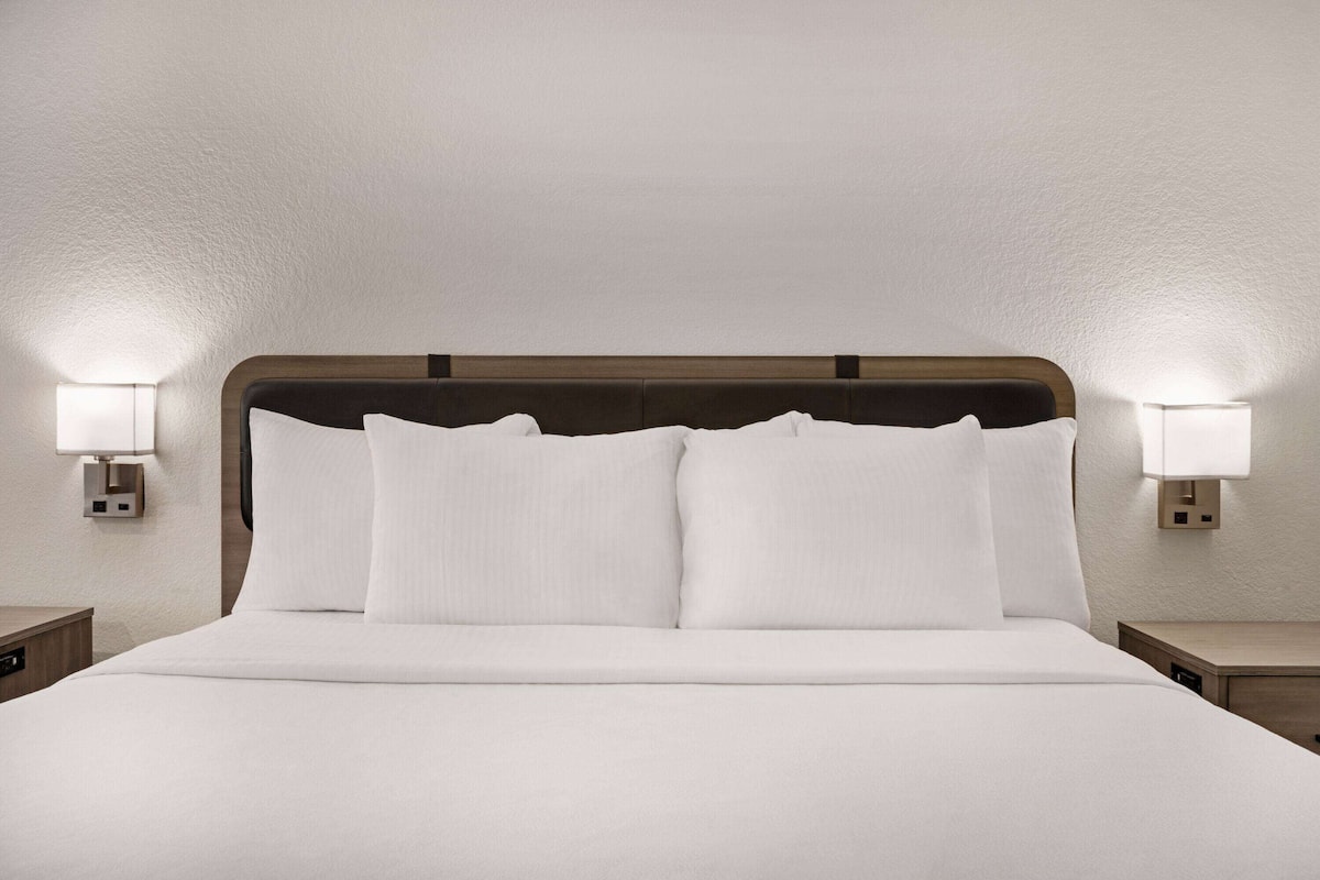 A neatly made bed with white linens, two bedside lamps, and a wooden headboard.