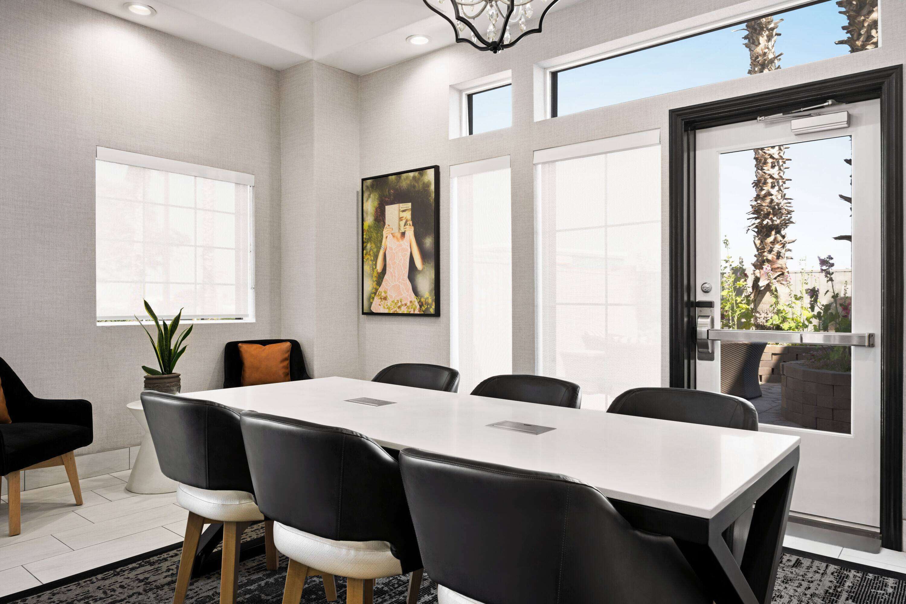 A conference room with a white table, black chairs, and a potted plant.