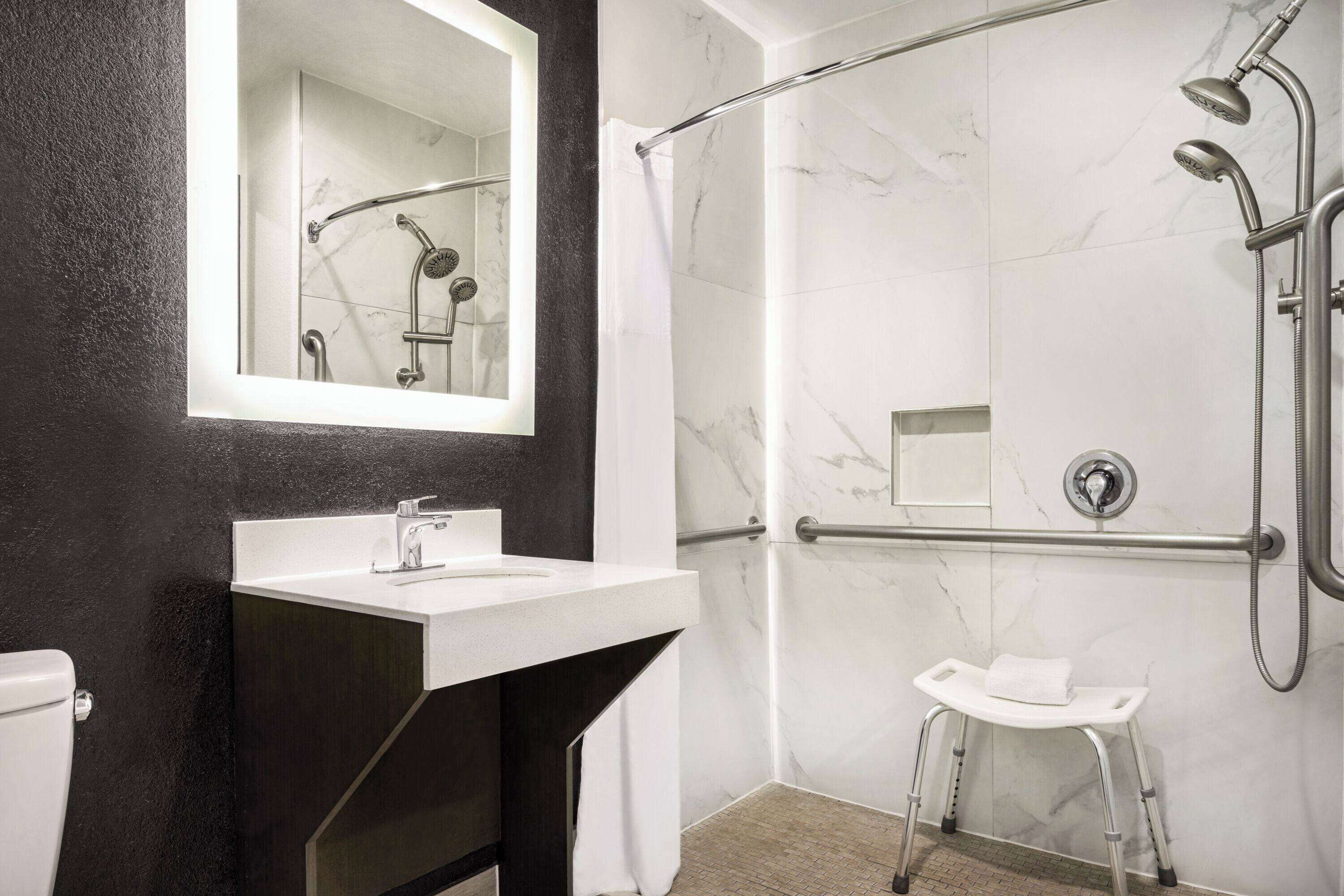 A modern bathroom with a marble shower, a white sink, and a small stool.
