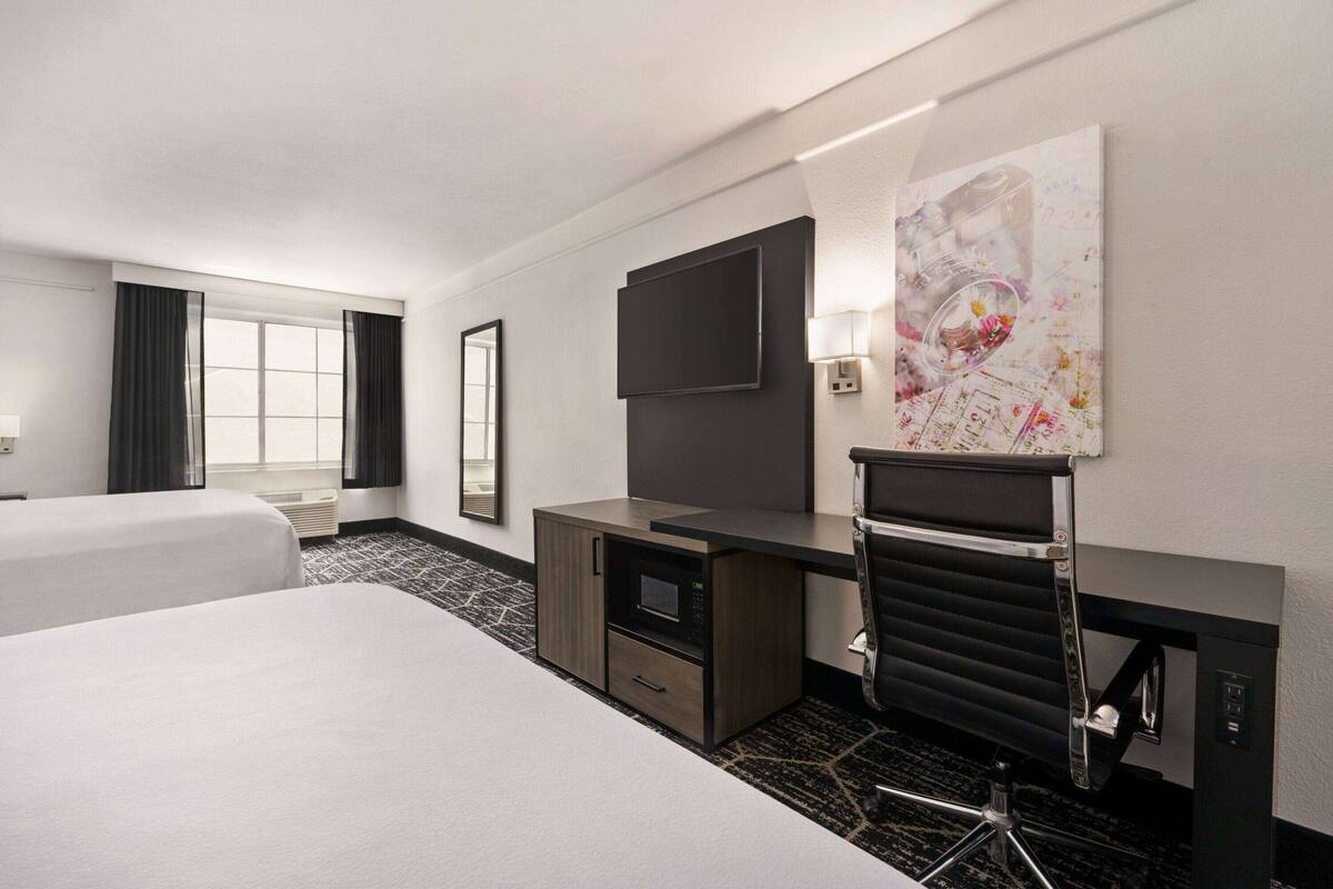 A hotel room with two beds, a desk with a flat-screen TV, a microwave, and a large abstract painting on the wall.