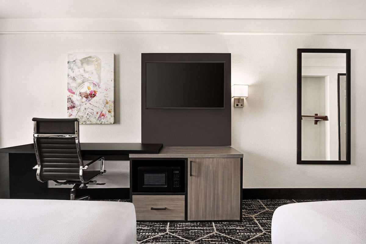 A hotel room with a desk, a chair, a bed, a TV, a microwave, and a mirror.