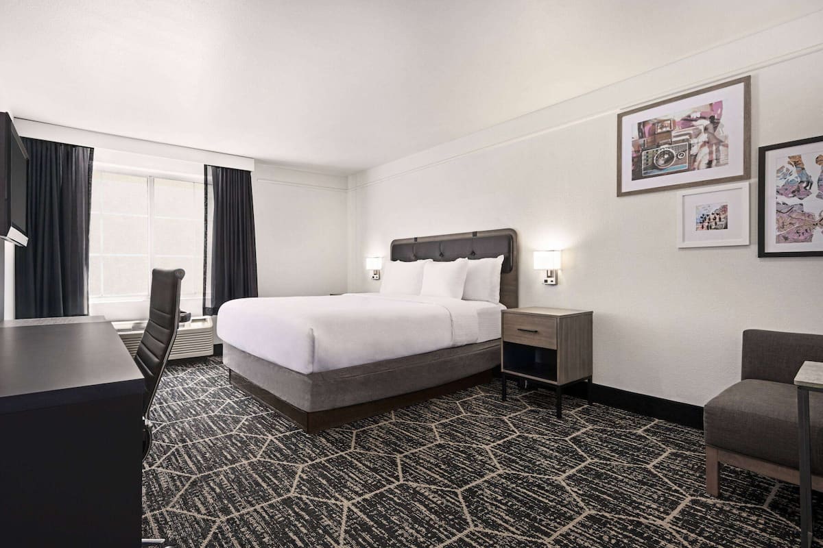 A hotel room with a bed, desk, chair, and a large window with curtains.