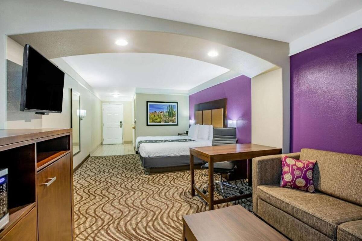 A hotel room with a bed, a desk, a sofa, a television, and a patterned carpet.