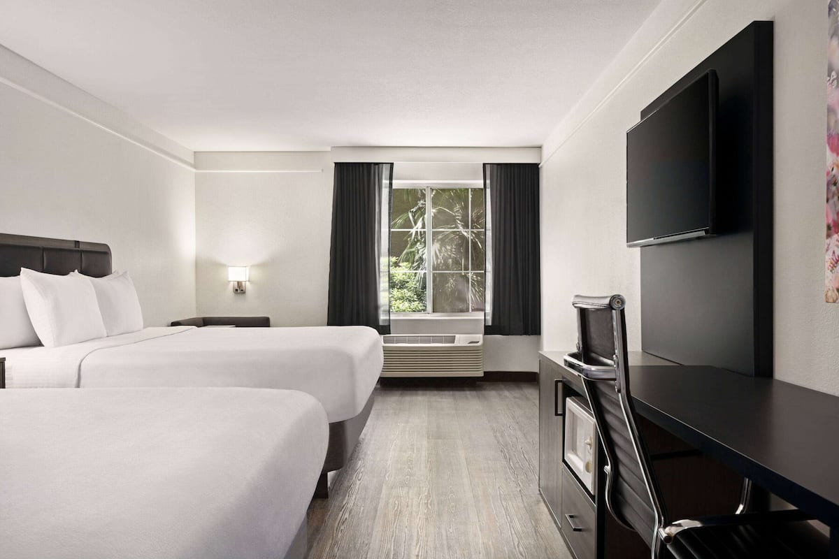 A hotel room with two beds, a TV, a desk, and a window with curtains.