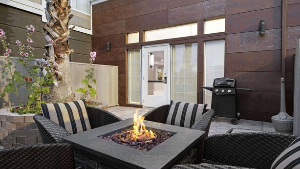 Un patio con un pozo de fuego cuadrado rodeado de muebles de mimbre y cojines a rayas.