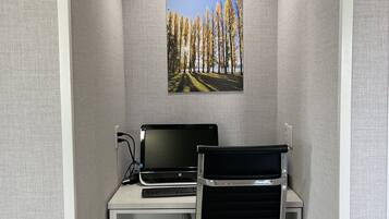 A small office space with a white desk, a black office chair, a laptop, and a framed picture of trees on the wall.