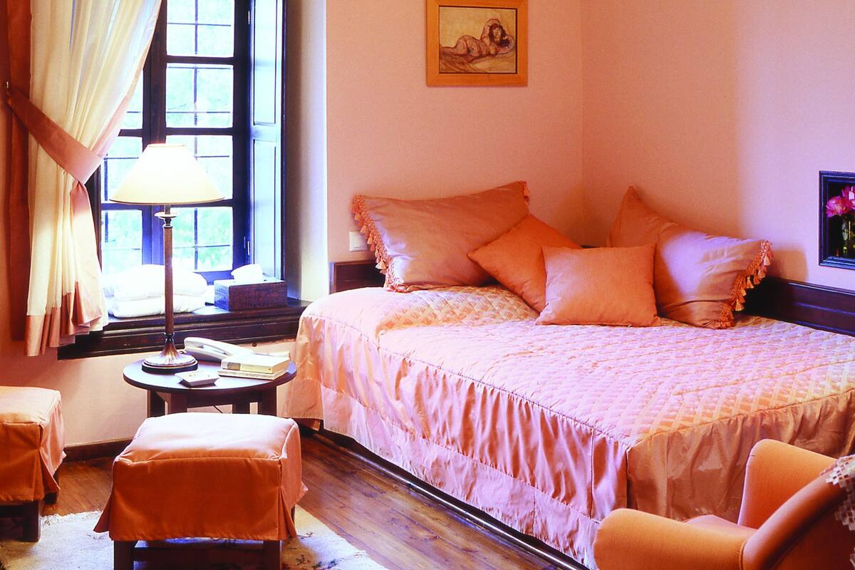 A bedroom with a bed, a chair, a table, a lamp, and a window with curtains.