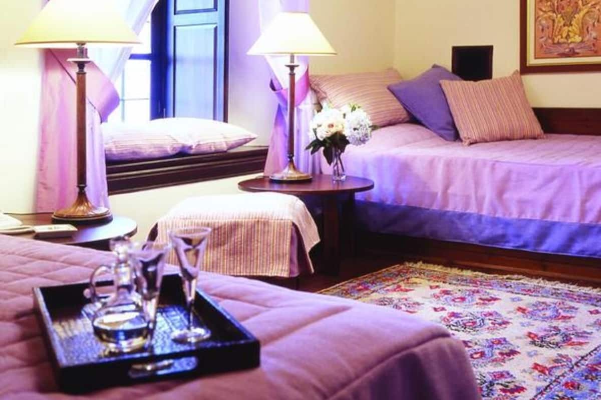 A hotel room with two beds, a chandelier, a painting, and a tray with glasses.