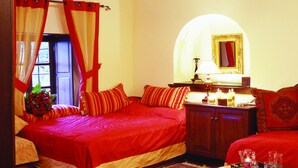 A bedroom with a large bed, a wooden ceiling, a chandelier, a mirror, and a bedside table with candles. - Santikos Mansion (South Pelion)