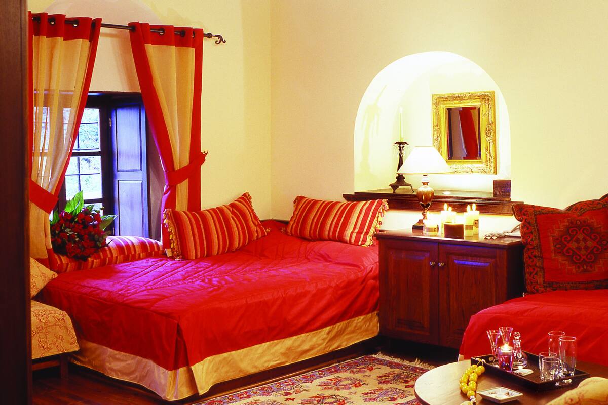 A bedroom with a large bed, a wooden ceiling, a chandelier, a mirror, and a bedside table with candles.