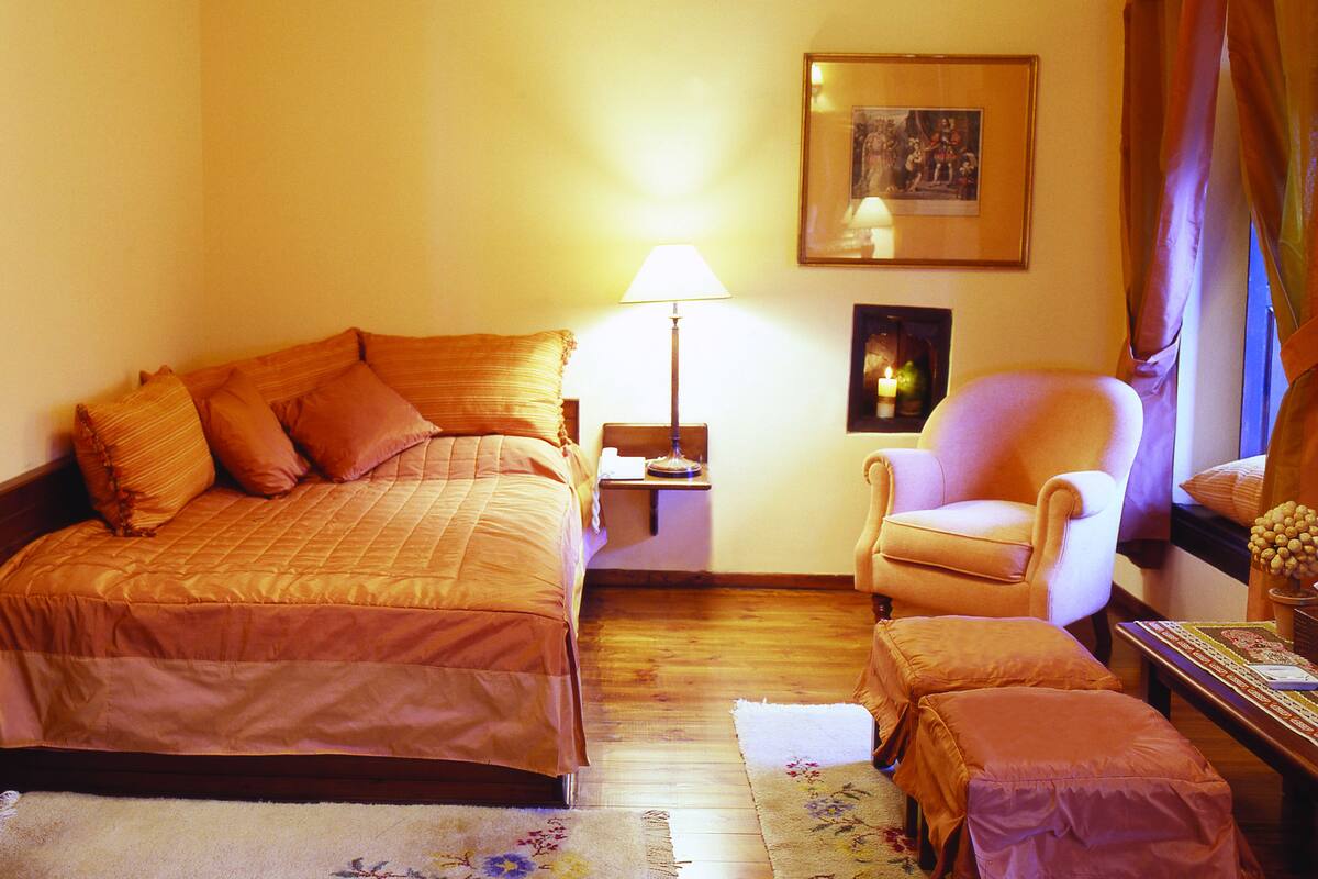 A hotel room with a bed, a chair, a nightstand, a lamp, and a framed picture on the wall.