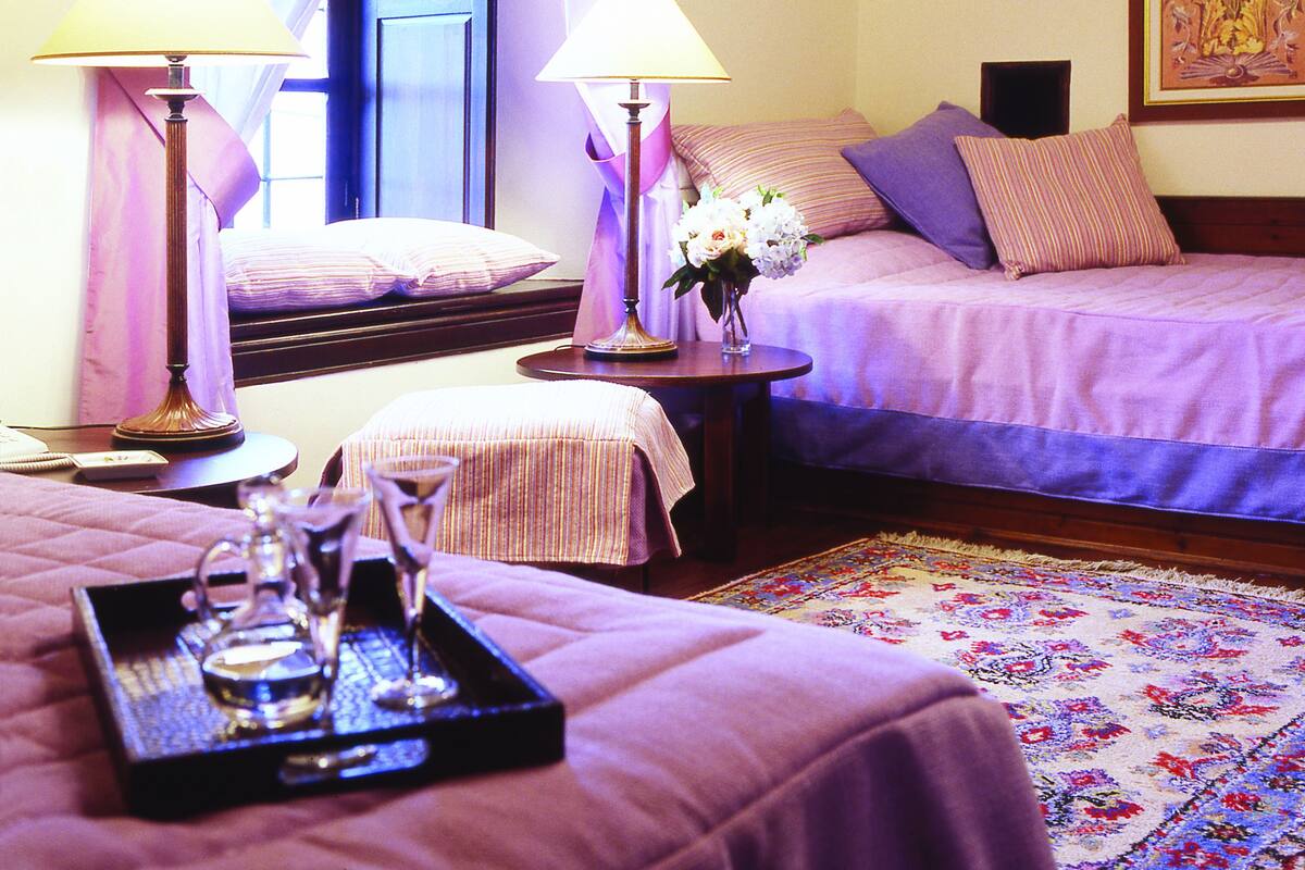 A hotel room with two beds, a chandelier, a painting, and a tray with a teapot and glasses.