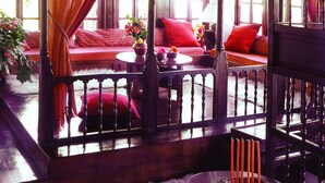 A room with a wooden ceiling, a red sofa, orange curtains, and a window with a stained glass design. - Santikos Mansion (South Pelion)