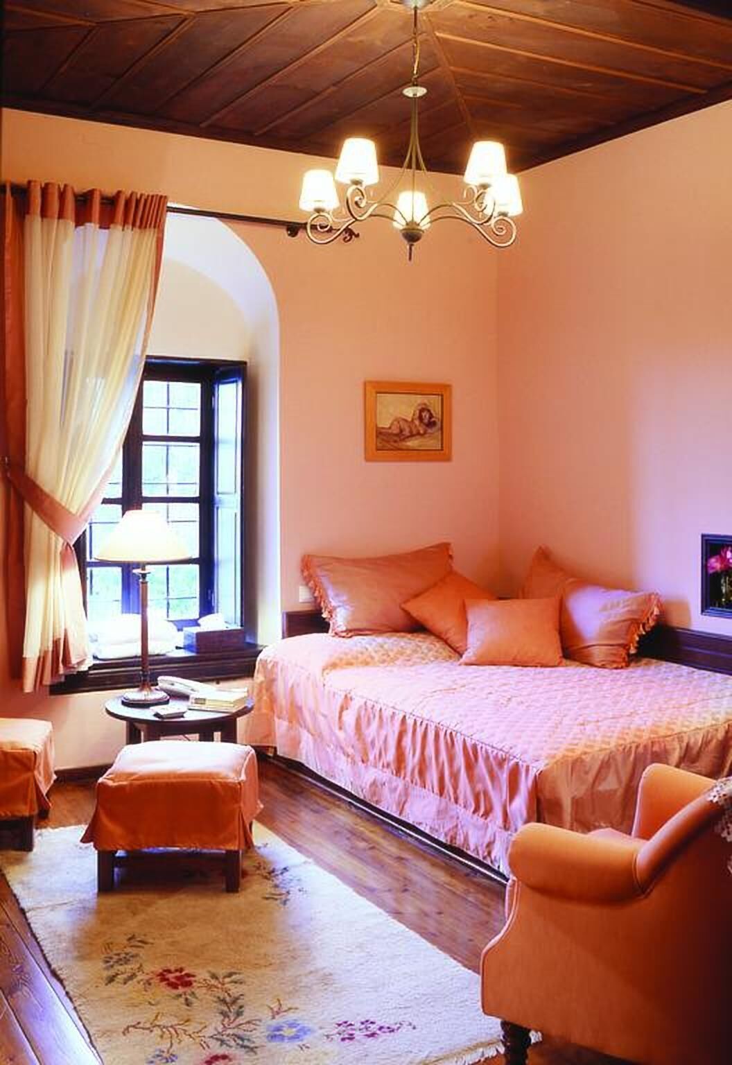 A bedroom with a bed, a nightstand, a lamp, a chair, and a window with curtains.