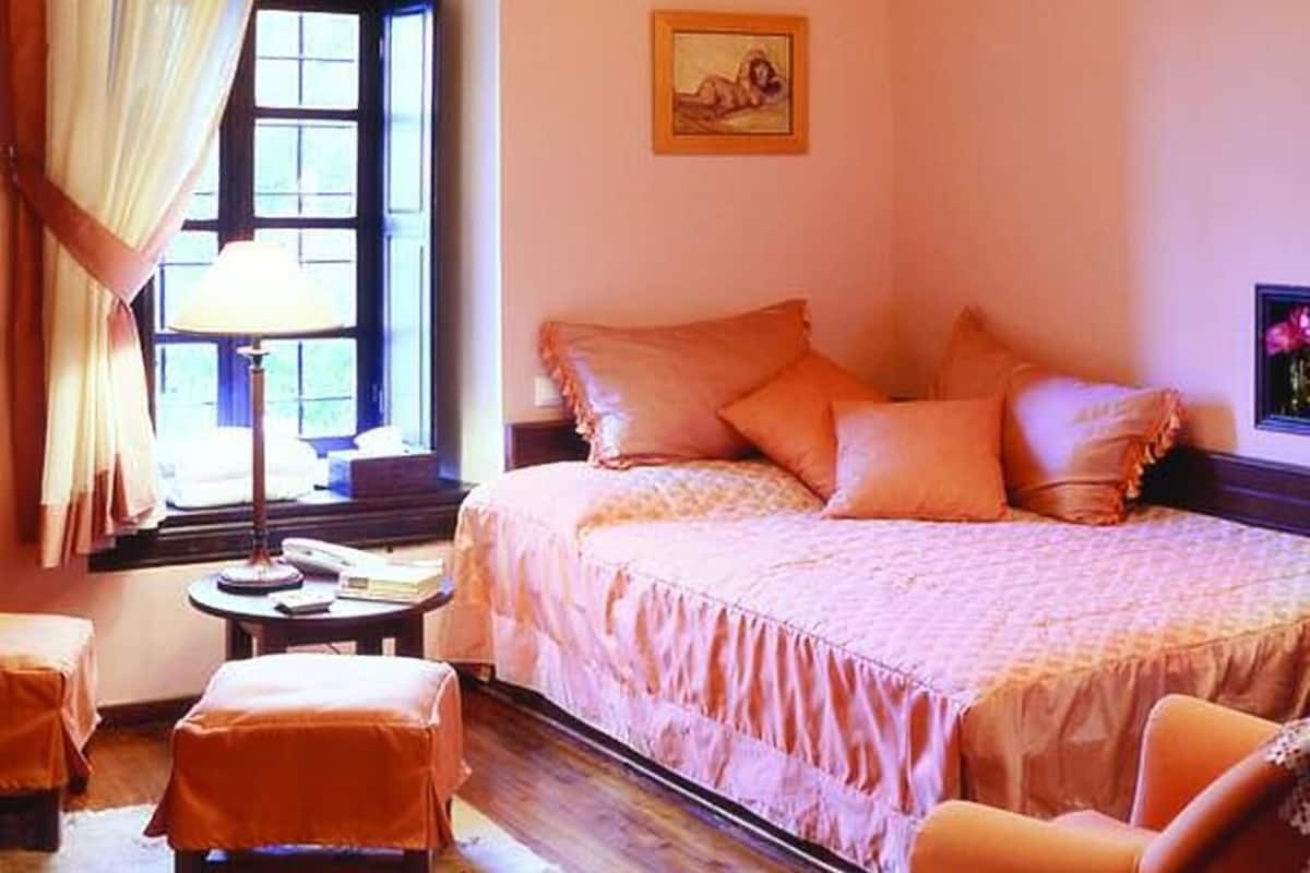 A bedroom with a bed, a nightstand, a lamp, a chair, and a window with curtains.