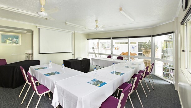 A conference room with white tables, purple chairs, and ceiling fans. - Seahaven Resort (Belgian Gardens)