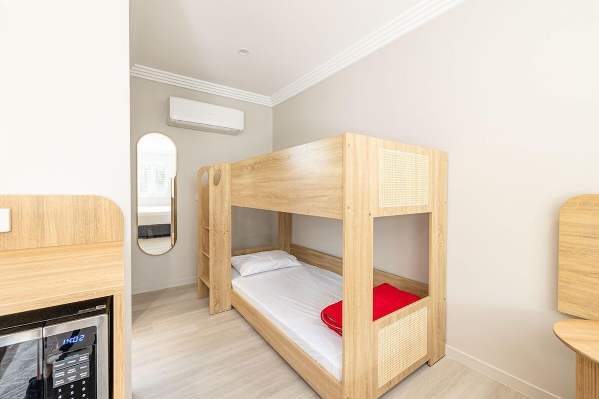 A bunk bed with a red pillow, a small table, and a mirror on the wall.
