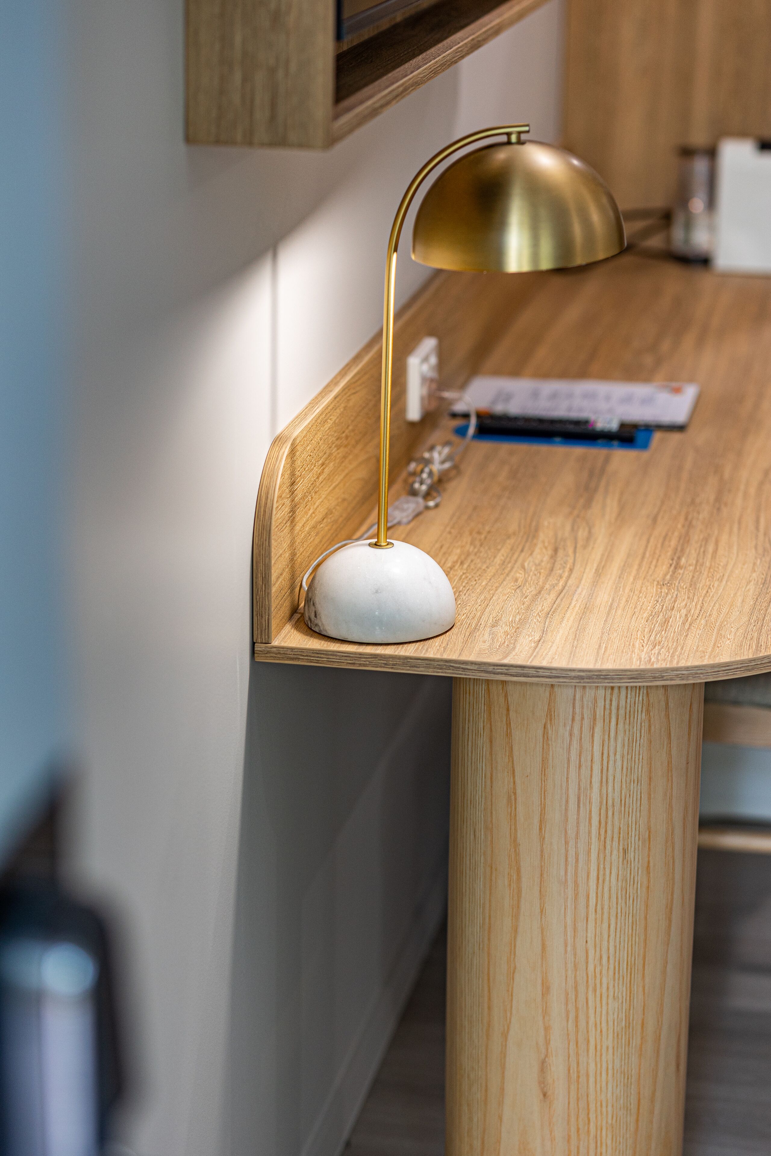 Un bureau en bois avec un socle en marbre blanc, une lampe de bureau dorée, ainsi que quelques papiers et un stylo posés sur le dessus.