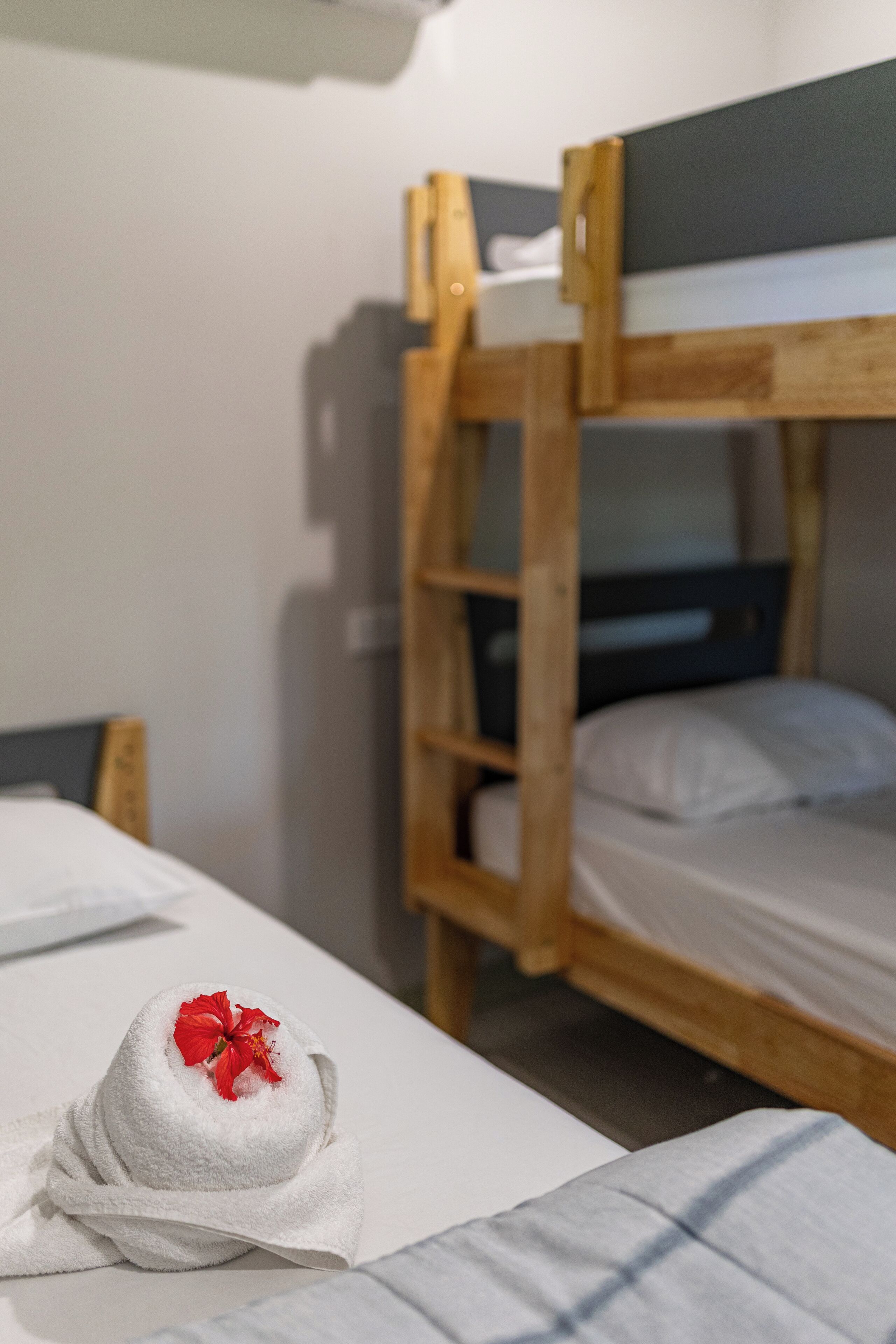 A room with bunk beds and a neatly made bed with a towel and a red flower.