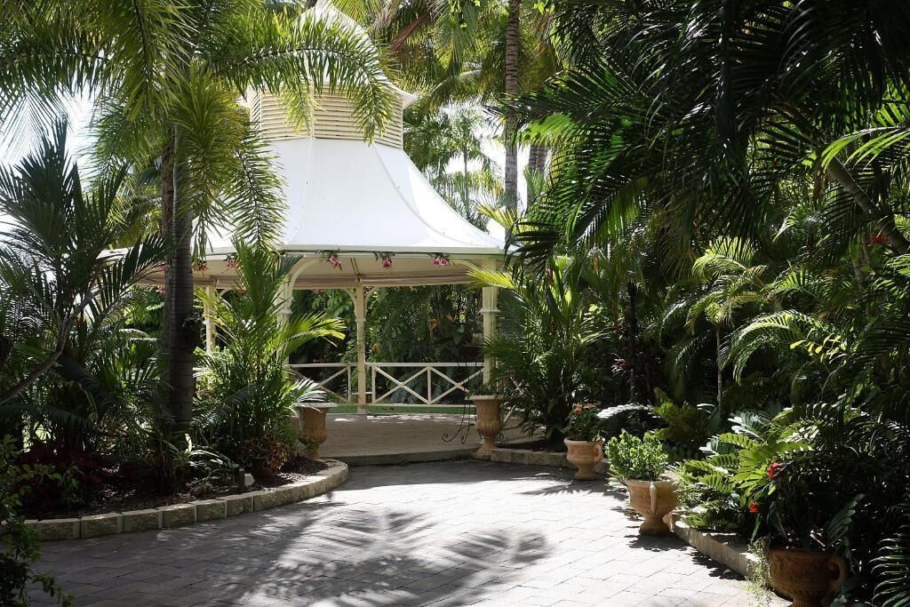 Um gazebo coberto, rodeado por vegetação tropical exuberante e um caminho pavimentado.