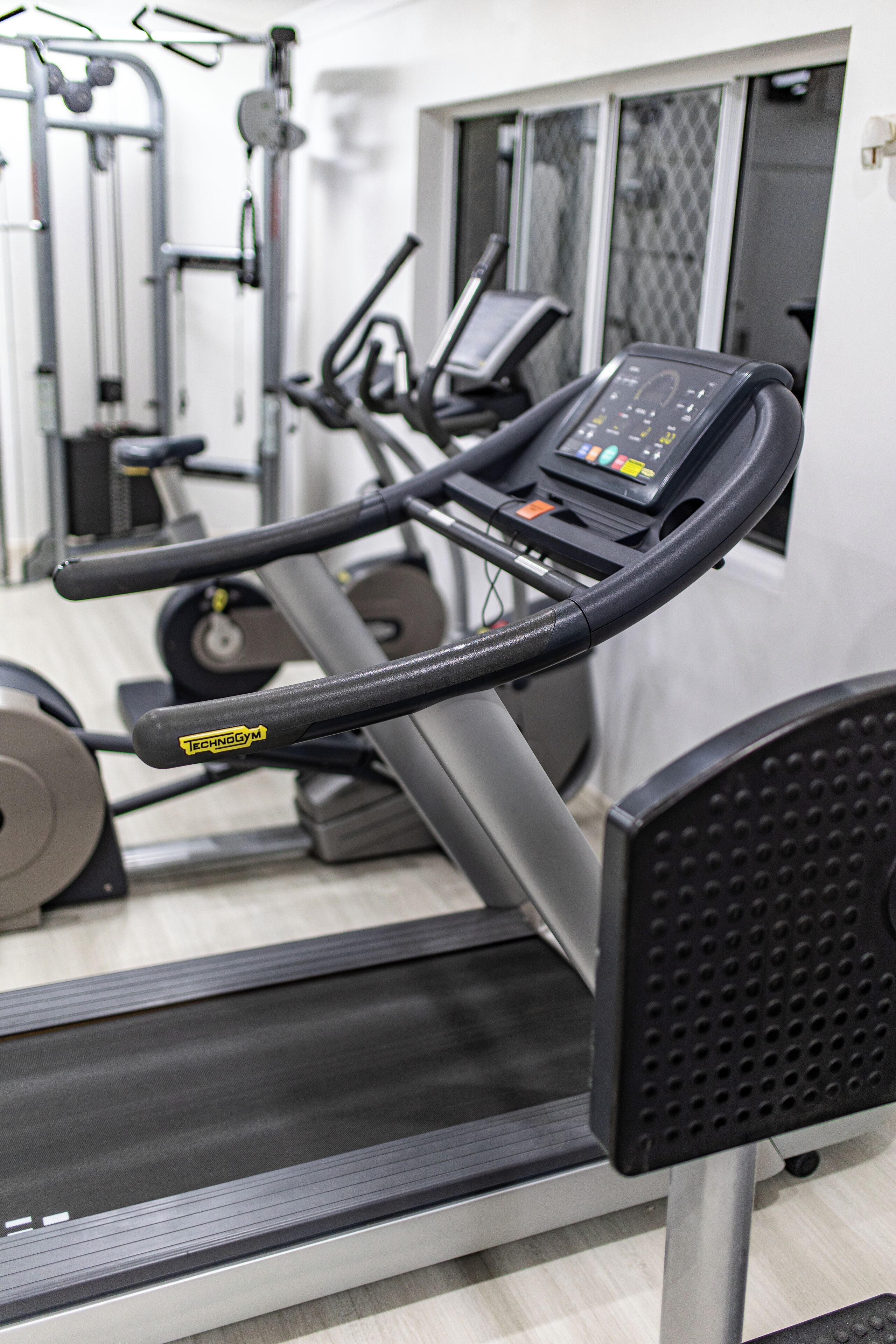 A gym with a treadmill, weight machines, and a mirrored wall.