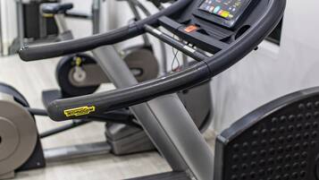 Une salle de sport équipée d’un tapis de course, d’appareils de musculation et d’un mur recouvert de miroirs.