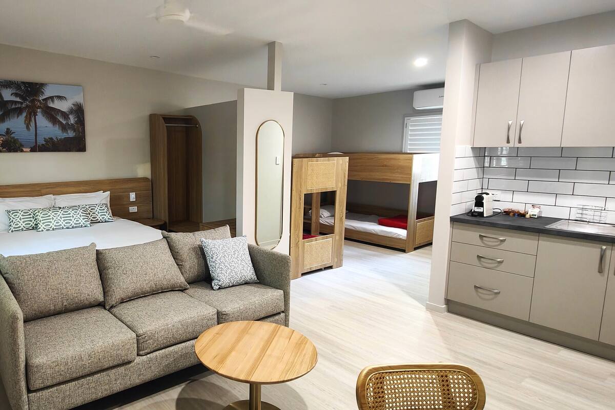 A hotel room with a bed, a sofa, a small round table, a kitchenette, and a bunk bed.