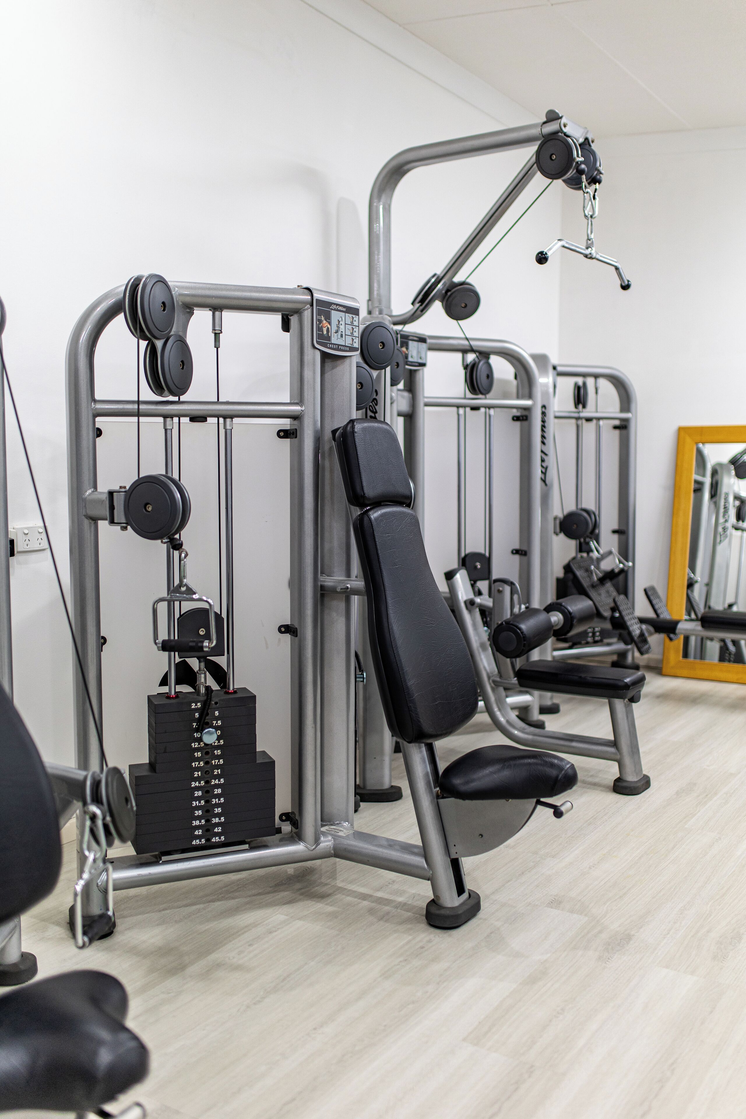 A gym with weight machines, benches, and a mirror.