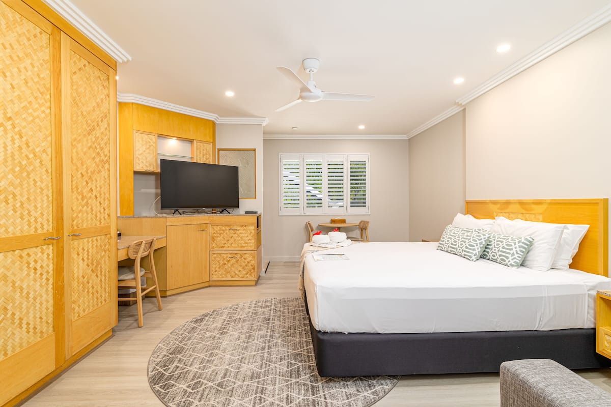 A hotel room with a bed, a desk, a television, and a window with shutters.