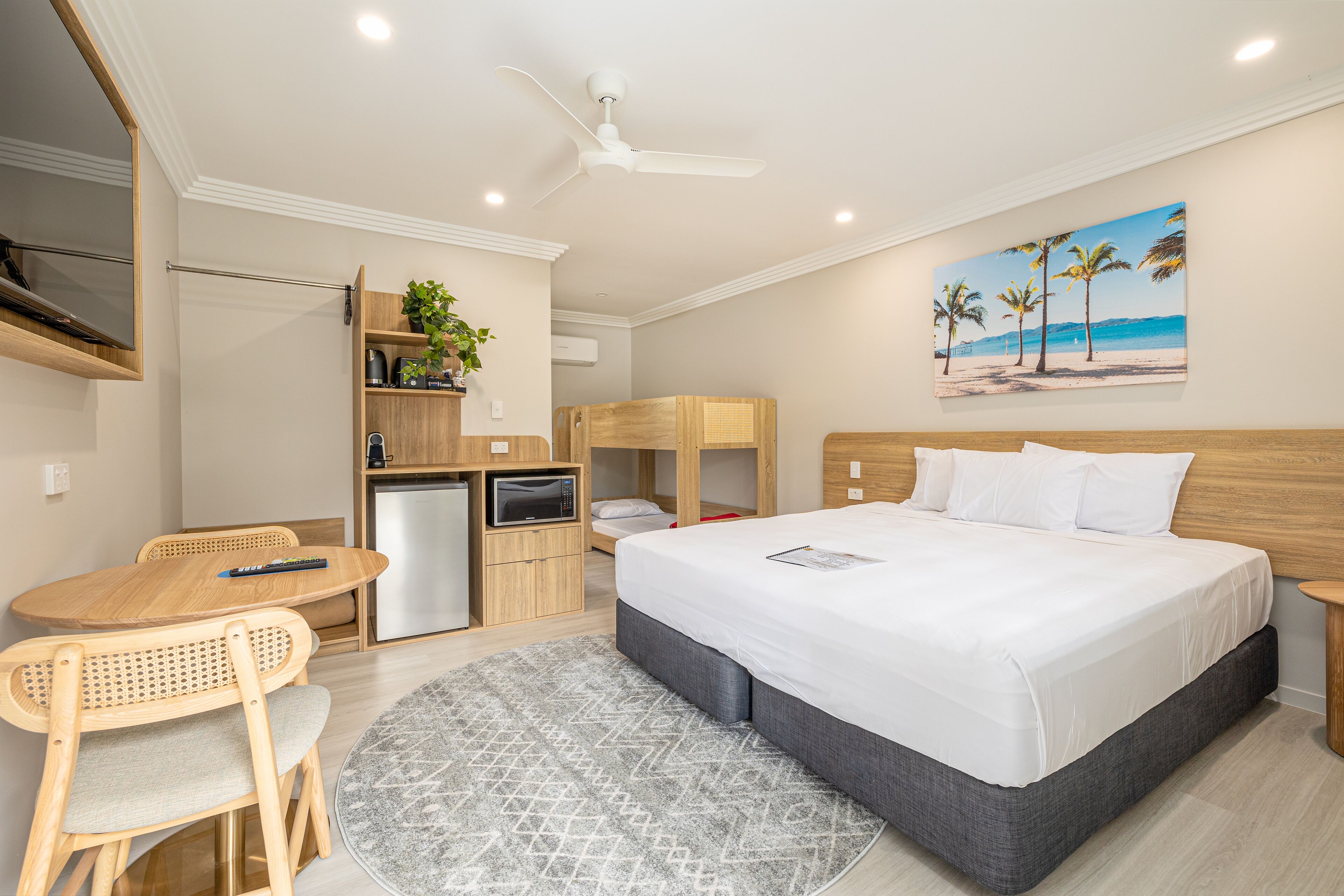 Habitación de hotel con cama, escritorio, silla, microondas, televisor y un cuadro de una playa.