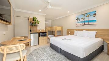Habitación de hotel con cama, escritorio, silla, microondas, televisor y un cuadro de una playa.