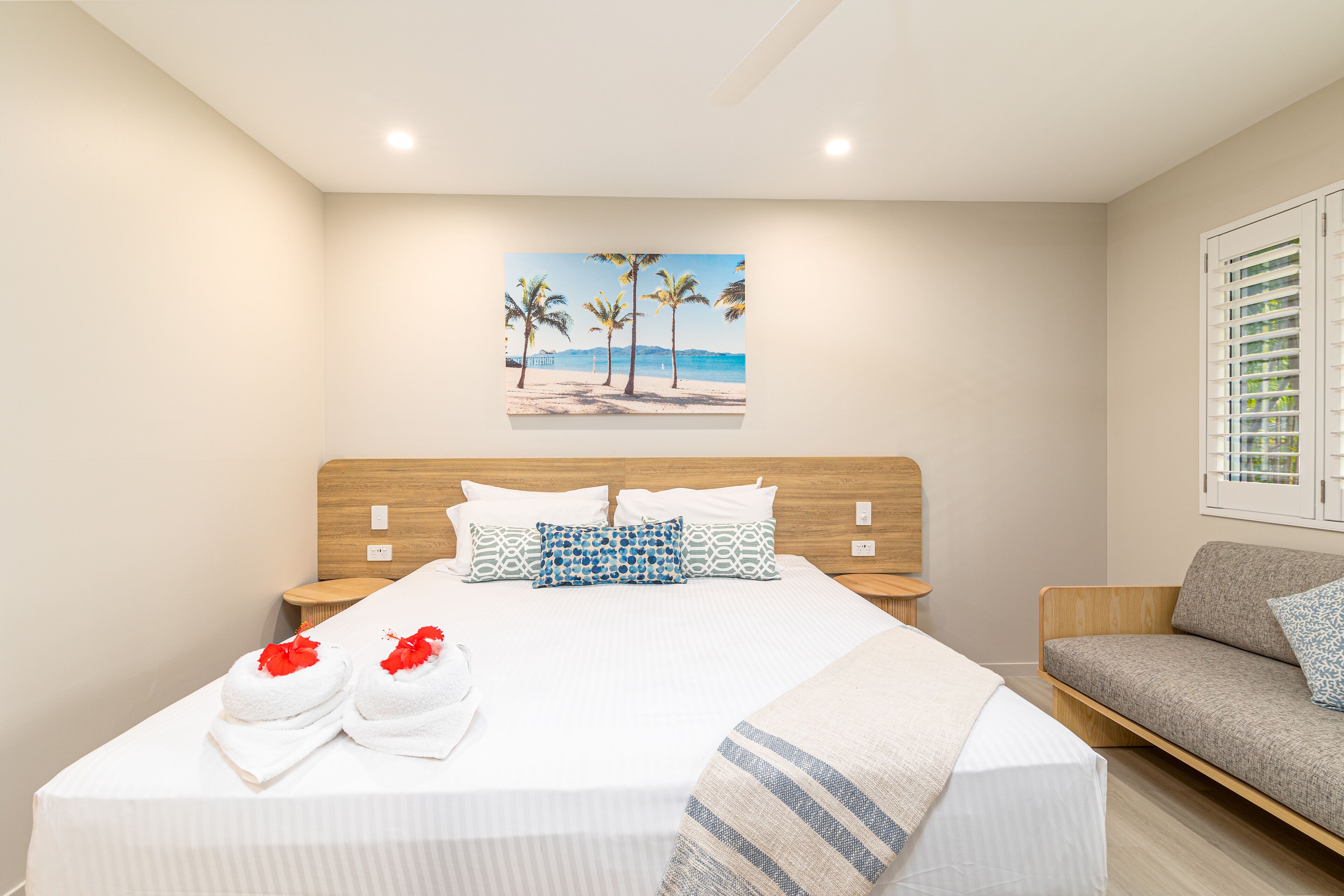 A hotel room with a bed, a wooden headboard, a painting of a beach, and a sofa.