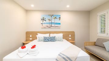A hotel room with a bed, a wooden headboard, a painting of a beach, and a sofa.