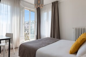 A modern hotel room with a large bed, a view of the city through a balcony, a dining table, and a radiator. - The Originals City, Hôtel Notre Dame, Rouen (Rouen)