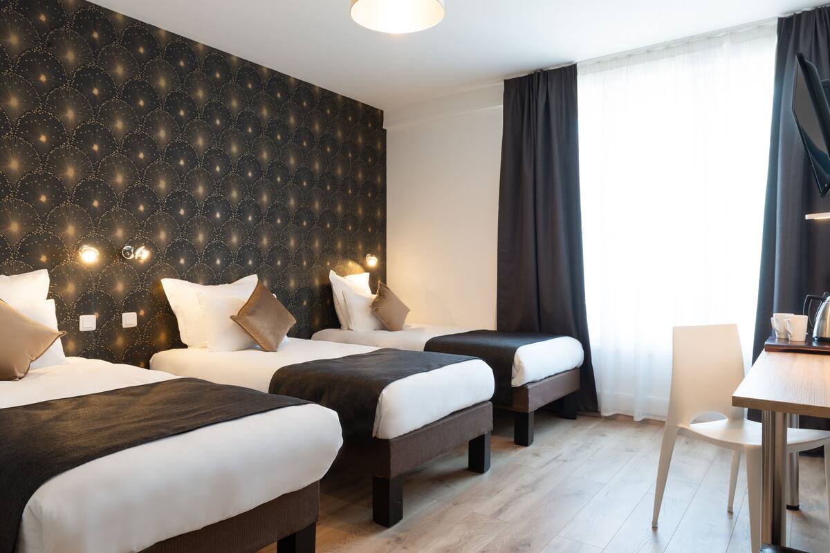 Une chambre d’hôtel avec trois lits, une table à manger et une grande fenêtre avec des rideaux.
