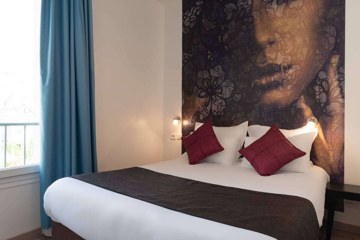 Un lit bien fait, avec du linge de lit blanc et marron, des oreillers rouges et une tête de lit sombre.