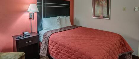 A hotel room with a bed, a nightstand with a lamp, a telephone, and a chair.