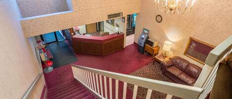 A hotel lobby with a reception desk, a staircase, a chandelier, and a brown leather sofa.